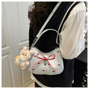 Détail du sac bandoulière en tissu bleu clair avec nœuds rouges et breloque chien