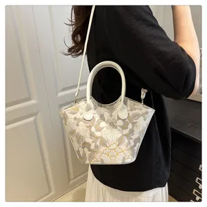 Detail of white floral embroidery on a minimalist crossbody bucket bag with gold hardware