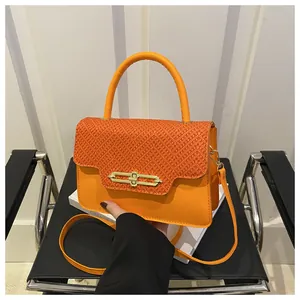 Close-up of orange leather handbag with textured flap and golden metal lock detail