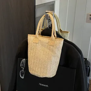 Straw bucket tote bag with herringbone weave and wide fabric handles on minimalist display