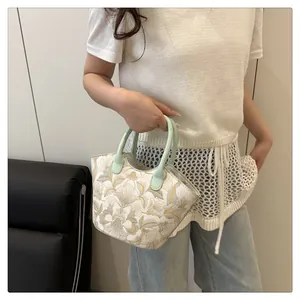 Detailed view of floral embroidery on a white crossbody bag with green round handles