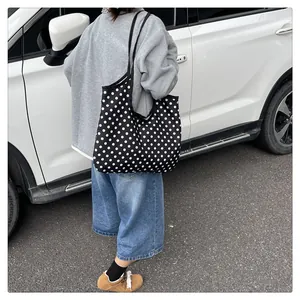 Close-up of black canvas tote bag with white polka dots carried over shoulder