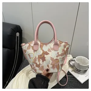 Detail of floral embroidery on a white trapezoid crossbody bag with pink leather handle