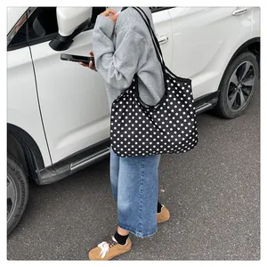 Detail view of a large black tote bag with white polka dots and wide shoulder strap