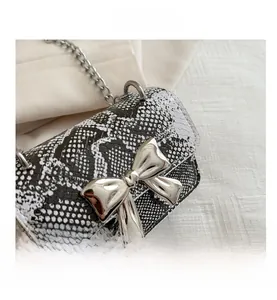 Detailed close-up of snake print pattern and silver bow on the mini crossbody chain bag