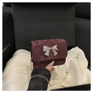 Detalle de mini bolso granate con textura de serpiente, lazo plateado y cadena fina