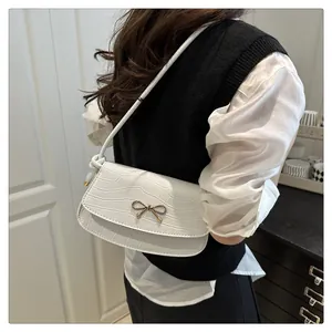 Detail of white crocodile-embossed crossbody bag with a golden bow-knot magnetic clasp