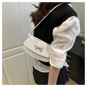 Detail of white crocodile pattern shoulder bag with golden metal bow accessory