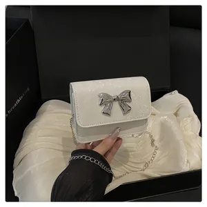 Primer plano del mini bolso blanco con textura de serpiente y lazo metálico plateado