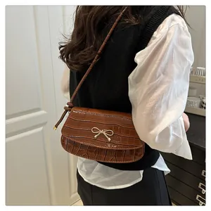 Detailed view of brown crocodile-textured shoulder bag with a gold bow buckle on a model