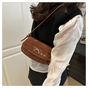 Detail of a brown croc-embossed square bag featuring a gold bow buckle on a crossbody strap