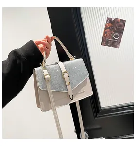 Detail einer beigen quadratischen Tasche mit silbernem Glitzer-Flap und Goldbeschlägen