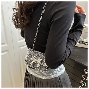 Detail showing the snake print texture and silver metal bow on a mini chain crossbody bag