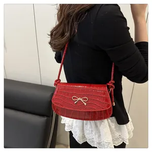 Detail view of red faux-leather crossbody bag with croc texture and golden bow