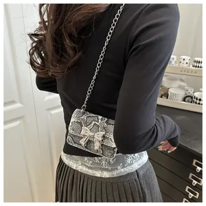 Detailed view of mini chain bag with snake print texture and silver bow buckle