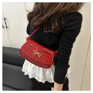 Close-up of the red faux crocodile leather shoulder bag with a gold bow buckle on a model