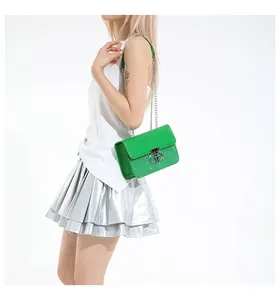 Detail of green sequin shoulder bag with silver chain and smooth leather flap on model
