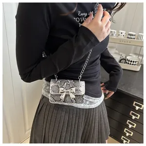 Detail of snake print mini crossbody bag featuring a silver metal bow and chain strap