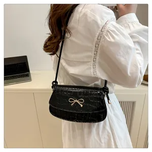 Detailed macro of black crocodile pattern embossing with golden bow hardware on crossbody bag