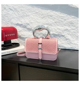 Détail d'un sac bandoulière rose tissé avec poignée métallique argentée et breloque cœur