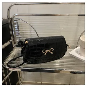 Close-up of black crocodile pattern leather bag with a golden metal bow buckle decoration
