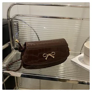 Close-up of brown crocodile texture leather bag featuring a gold bow metallic clasp