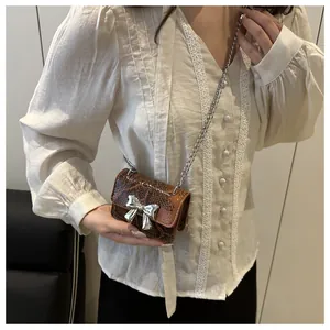Detail of mini crossbody bag in brown snakeskin texture with a silver bow clasp