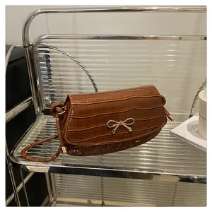 Detail of dark brown faux crocodile leather bag with gold bow clasp and shoulder strap