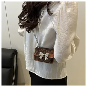 Detail of snake skin texture and metallic bow on mini crossbody bag with chain strap