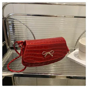 Detail of red crocodile pattern handbag featuring a gold bow buckle on display