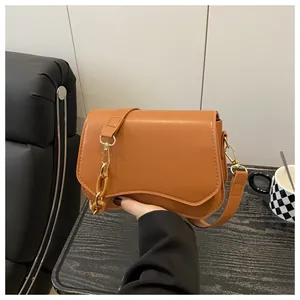 Detail of tan faux leather square bag featuring curved flap and gold chain strap