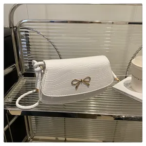 Detail of white crocodile-embossed mini bag with golden metal bow buckle on a shelf