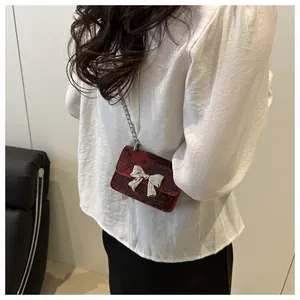 Close-up of a mini red snakeskin chain bag with a large silver bow on a female model