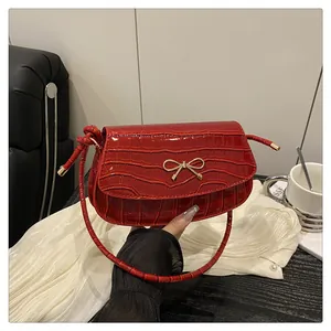 Detail of red crocodile pattern handbag featuring a gold bow clasp and elegant ribbon handle