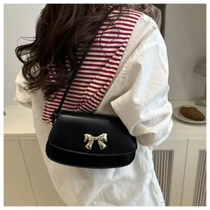 Détail du sac bandoulière noir tendance avec nœud doré porté par un mannequin