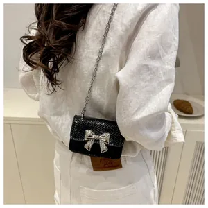 Detail of mini black crossbody bag with snake texture and large silver metal bow