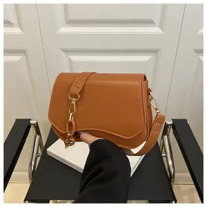 Detail of tan shoulder bag featuring wavy flap design and gold metal chain hardware