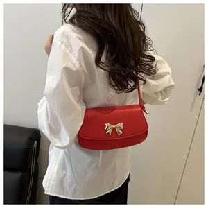 Détail d'un sac bandoulière en cuir rouge avec boucle nœud dorée sur chemise blanche