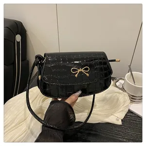 Detail of glossy black crocodile pattern shoulder bag with a gold bow metal hardware