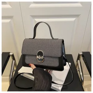 Close-up of a small square handbag with grey woven texture and black leather details