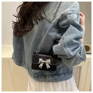 Detail of black mini square bag with snake texture and silver metal bow on blue denim