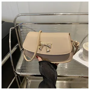 Détail du sac à bandoulière beige avec nœud doré et rabat en cuir au design élégant