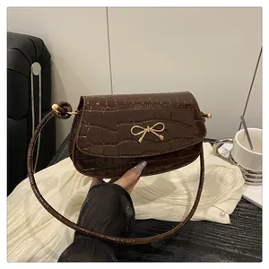 Detail of dark brown crocodile embossed texture and golden bow buckle on the handbag