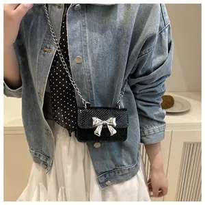 Detail of mini black crossbody bag featuring silver bow metal buckle and snake texture