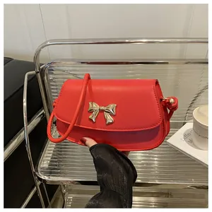 Détail d'un sac à bandoulière en cuir rouge avec un décor de nœud en métal doré