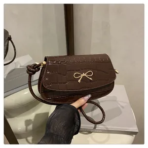 Detail of dark brown crocodile embossed crossbody bag with golden bow and knotted handle