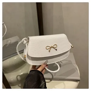 Detailed view of white faux crocodile leather texture and golden bow buckle on crossbody bag