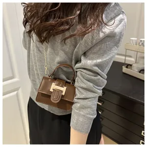 Detailed view of dark brown leather handbag with gold H buckle on a grey sweater
