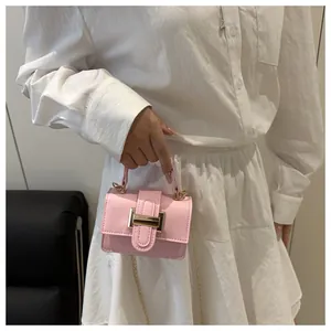 Detail shot of pale pink mini square bag with golden buckle and chain on white dress