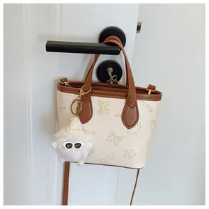 Detail of cream bucket bag with brown handles, floral prints and a fuzzy monster charm